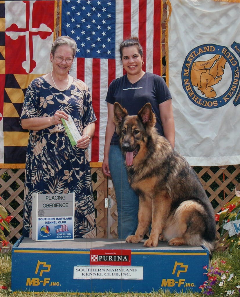 Denise Willis standing with her German Shepherd Chewy at a Southern Maryland Kennel Club obedience trial, beside a club official presenting a placing ribbon.